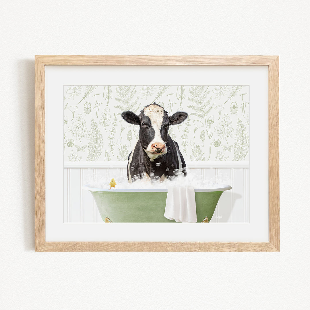 A black and white cow is sitting in a green bathtub filled with bubbles, with a towel draped over the side of the tub.