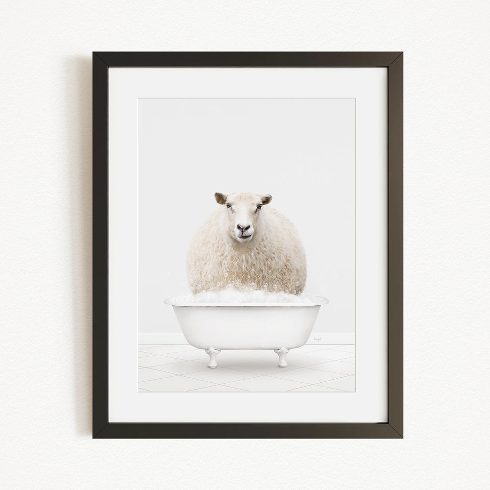 A fluffy white sheep sits in a white bathtub filled with bubbles, looking directly at the camera.