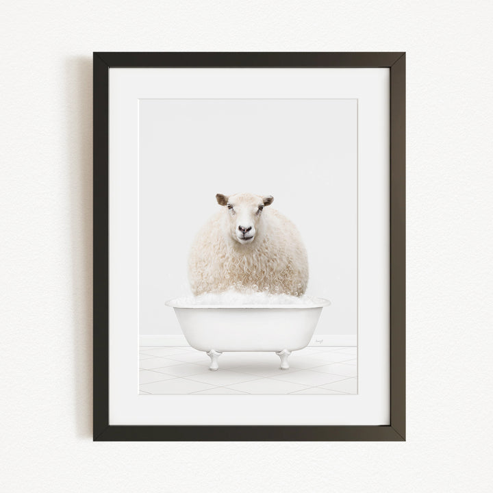A fluffy white sheep sits in a white bathtub filled with bubbles, looking directly at the camera.