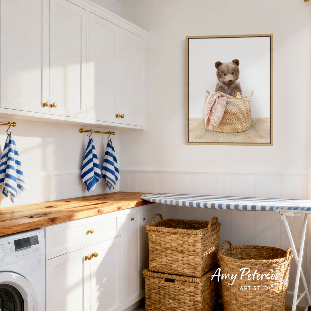 A cozy laundry room with white cabinets, a wooden countertop, and a framed image of a bear sitting in a basket.