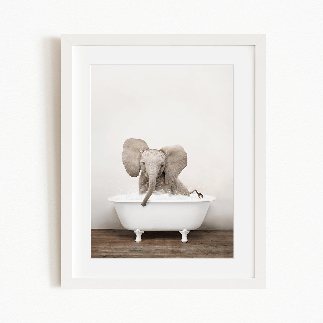 A baby elephant sitting in a white bathtub, with its trunk submerged in the water.