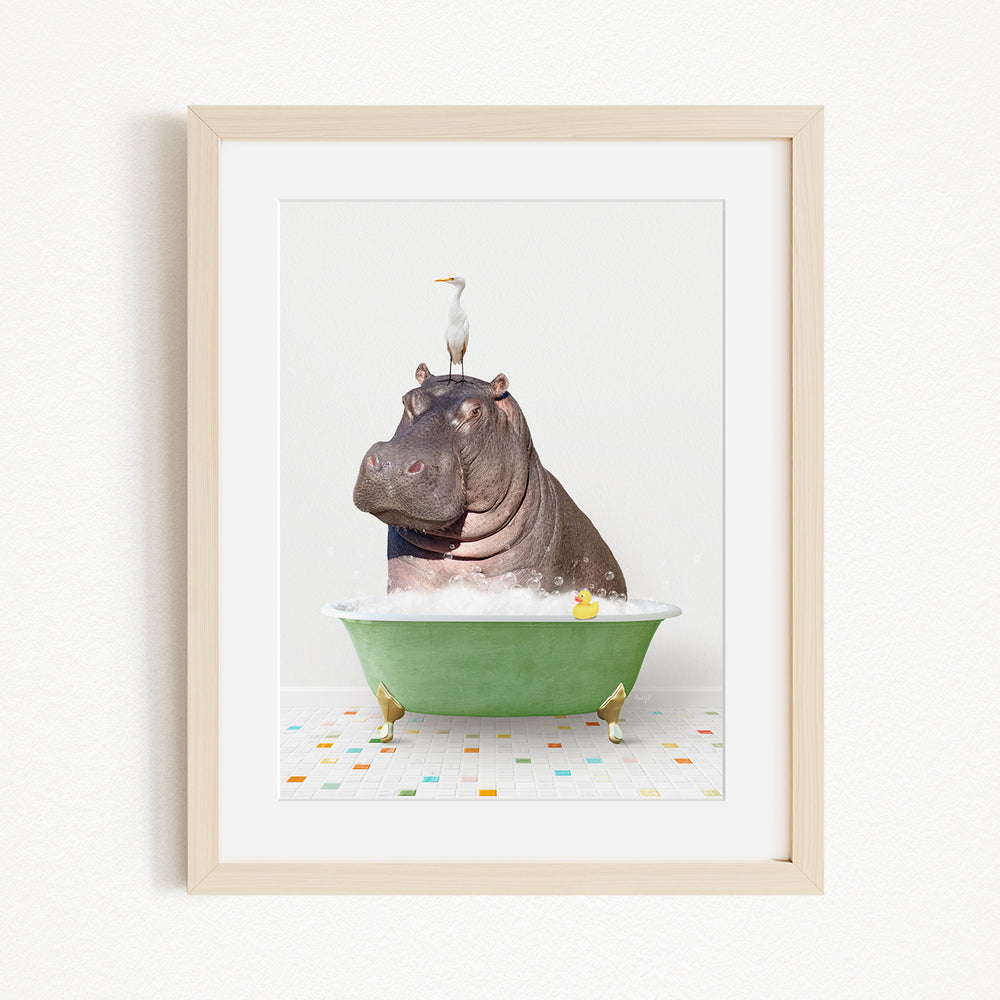 A framed image depicting a hippopotamus sitting in a green bathtub, with a bird perched on its head.
