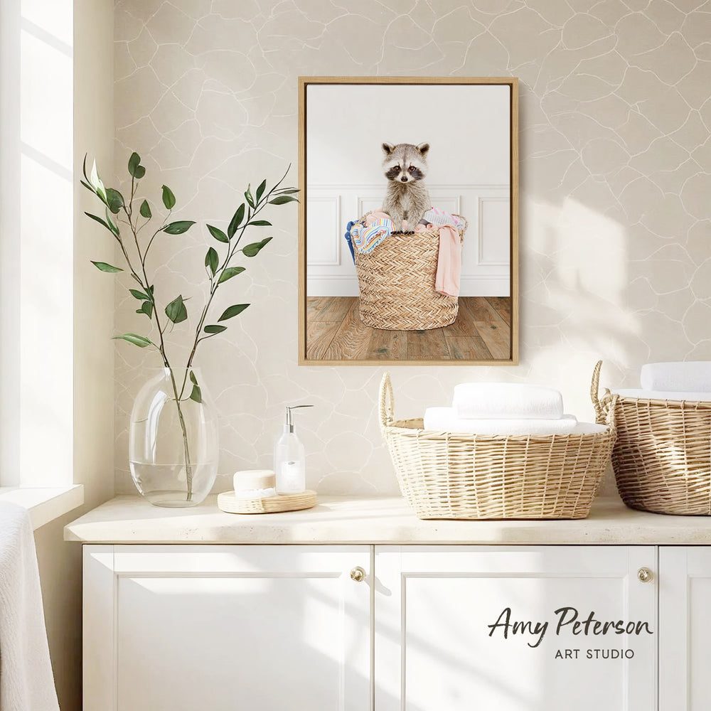 a raccoon sitting in a woven basket on a wooden floor, with a framed photo of the raccoon hanging on the wall above it.