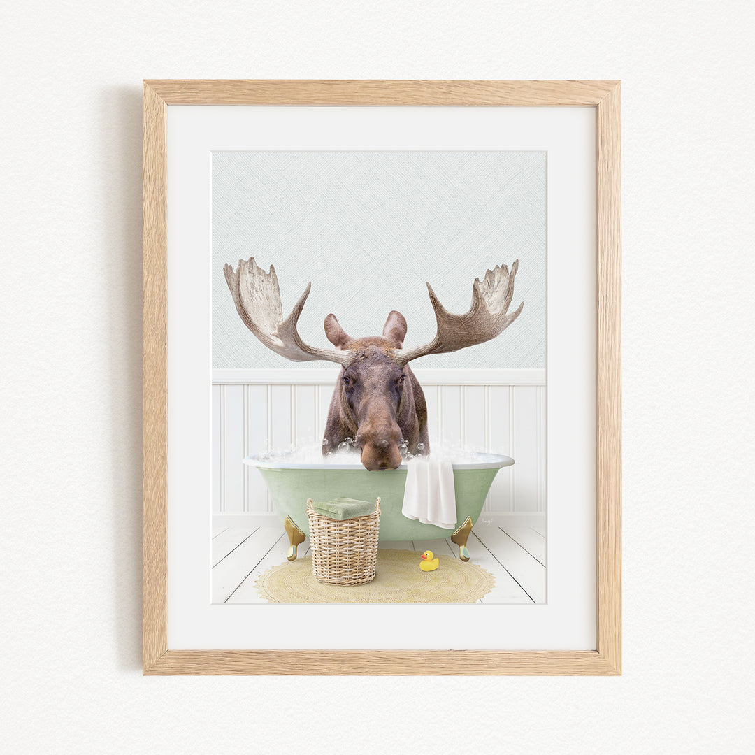 A framed image depicting a moose with large antlers sitting in a green bathtub, surrounded by a basket of rubber ducks and a yellow rubber ducky.