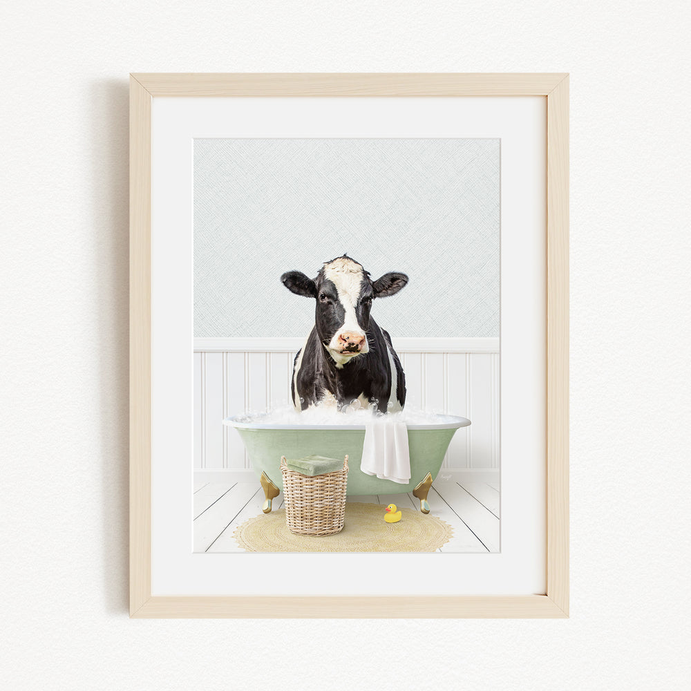 A black and white cow is sitting in a green bathtub filled with water, surrounded by rubber ducks and a basket.