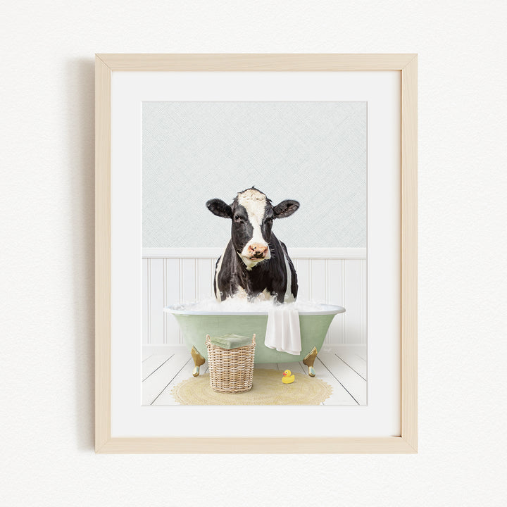 A black and white cow is sitting in a green bathtub filled with water, surrounded by rubber ducks and a basket.