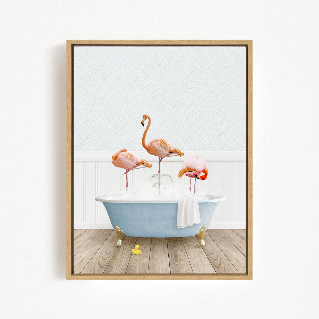 A framed image depicting three flamingos standing in a blue bathtub filled with bubbles, with a white towel hanging on the side.
