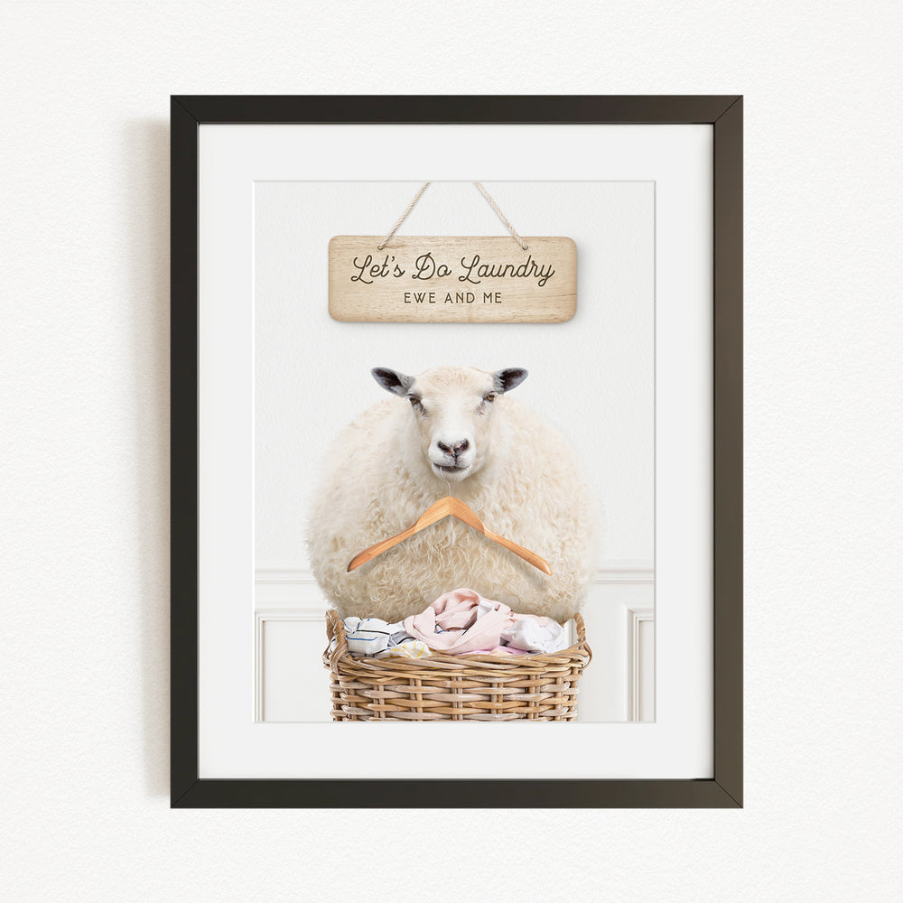 A framed image of a sheep sitting in a basket filled with laundry, with a sign above it that says "Let's Do Laundry EWS AND ME".