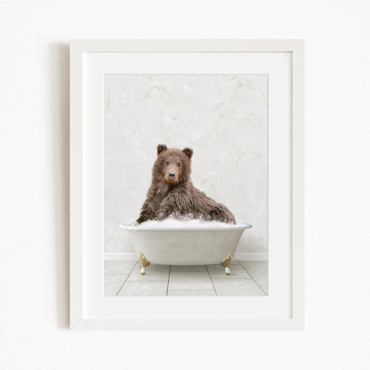 A brown bear sitting in a white bathtub filled with bubbles, looking directly at the camera.