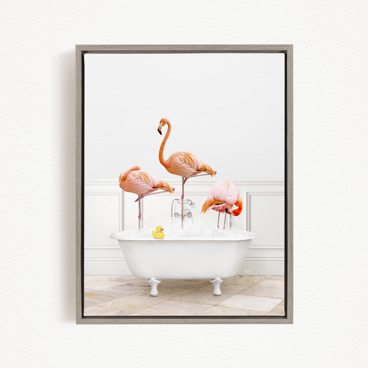 A framed image depicting three flamingos standing in a white bathtub filled with water, with a yellow rubber duck floating in the water.