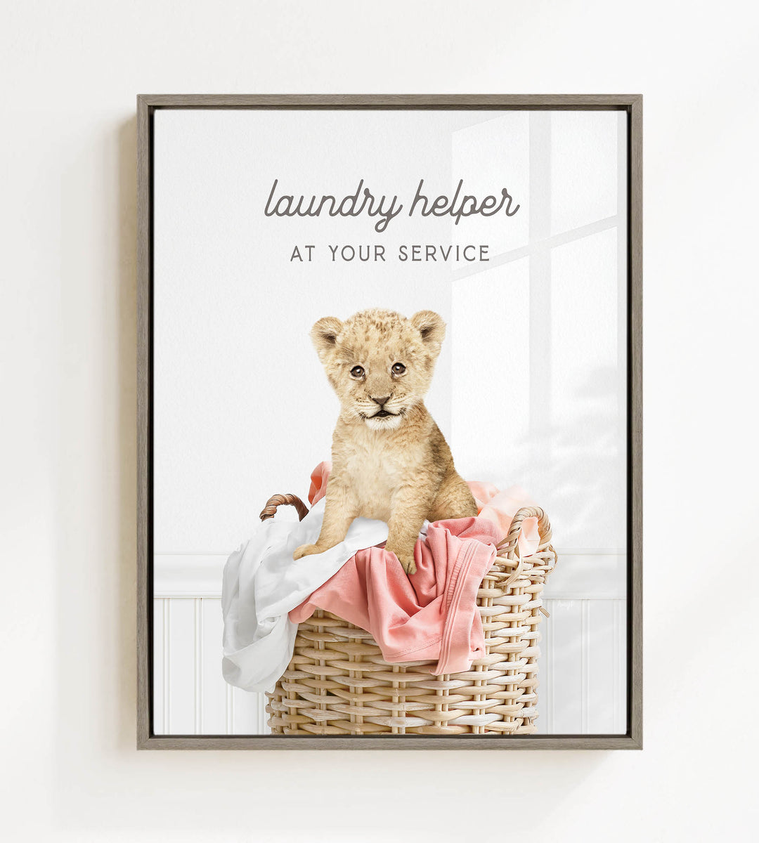 A young lion cub sitting in a wicker laundry basket, with a pink blanket and towels around it.