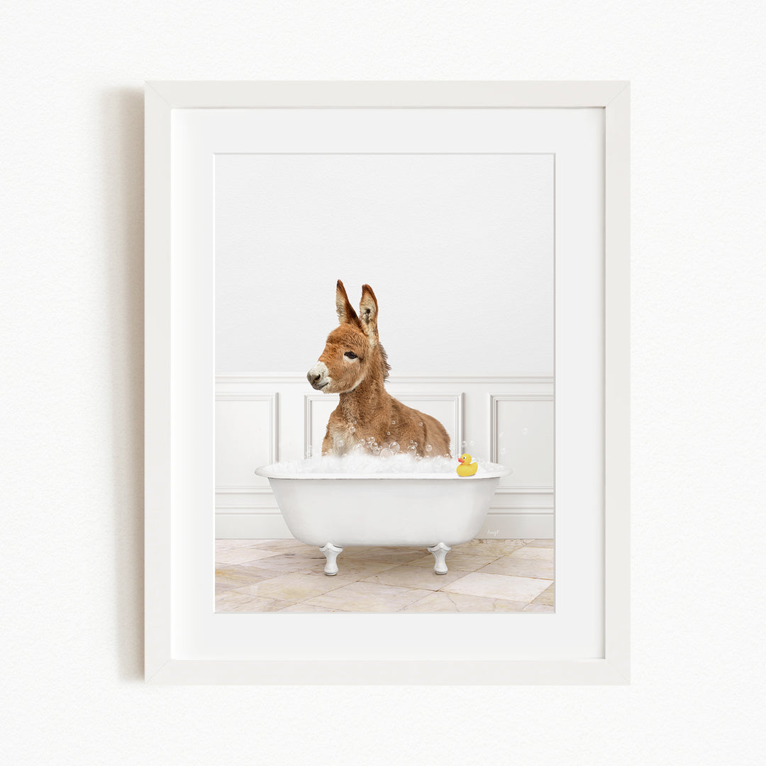 A donkey is sitting in a white bathtub filled with water, with a yellow rubber duck floating in the water.