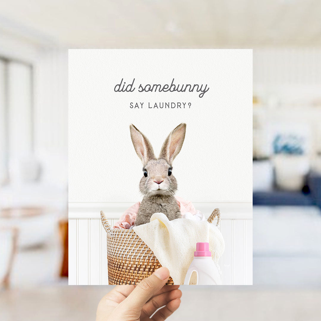 A hand holding a card with a picture of a rabbit sitting in a basket filled with laundry, with the text "did some bunny Say laundry?"