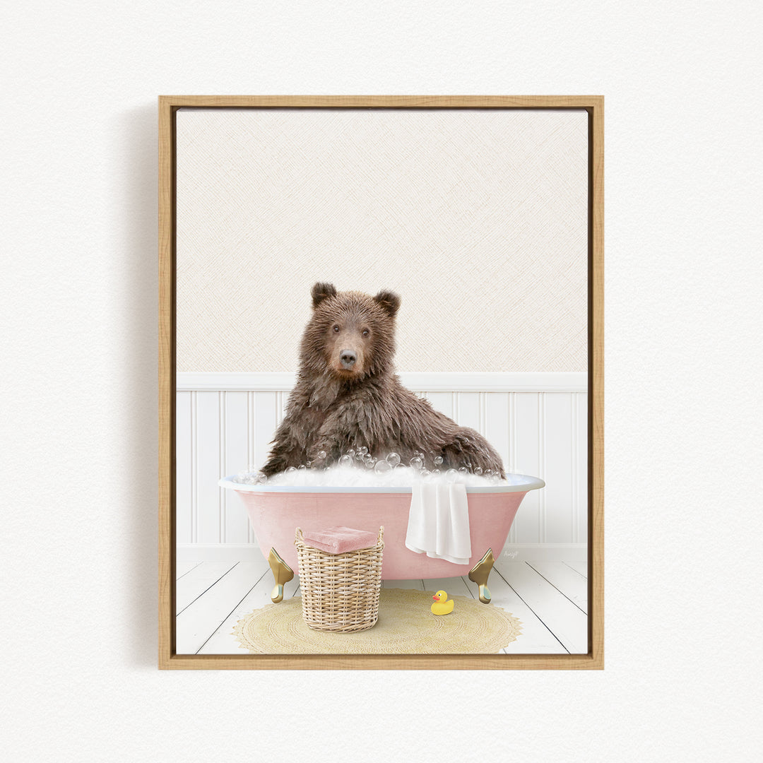 A brown bear sitting in a pink bathtub filled with bubbles, surrounded by a yellow rubber duck and a wicker basket.