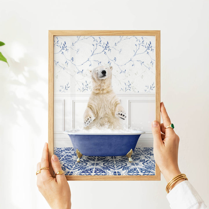 A person's hands are holding a framed picture of a polar bear sitting in a blue bathtub, surrounded by a blue and white floral pattern.