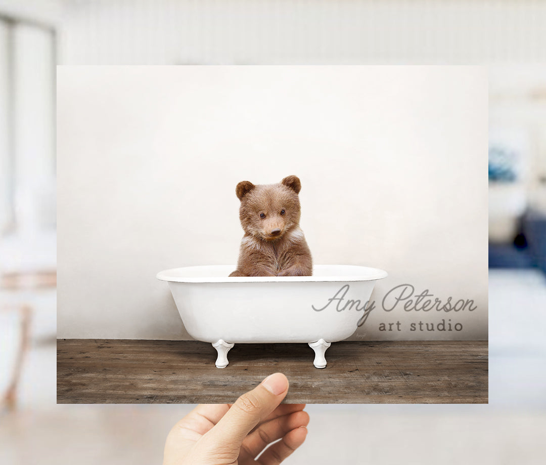 a hand holding a photo of a teddy bear in a bathtub