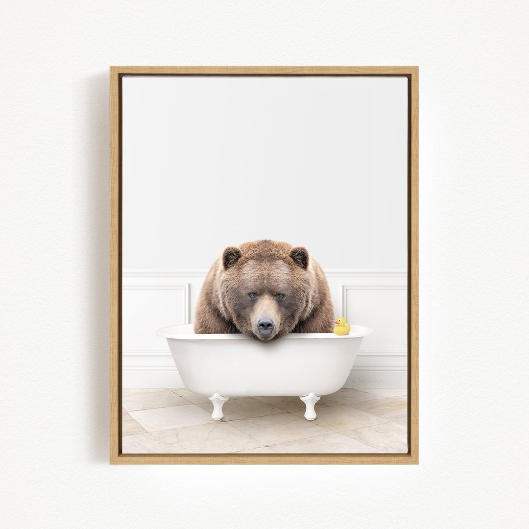 A brown bear is sitting in a white bathtub, with a yellow rubber duck floating in the water.