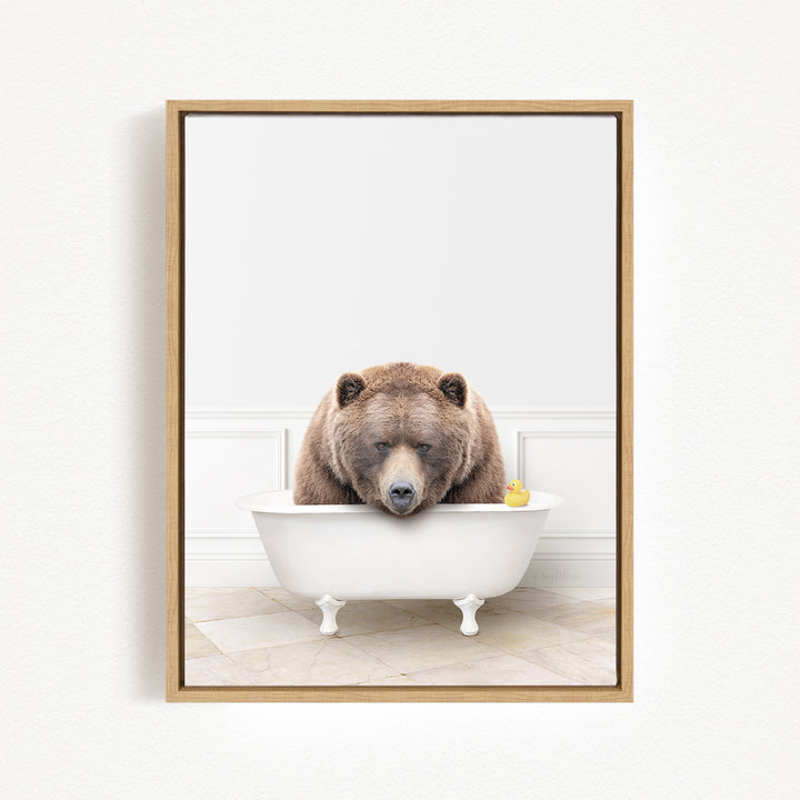 A brown bear is sitting in a white bathtub, with a yellow rubber duck floating in the water.