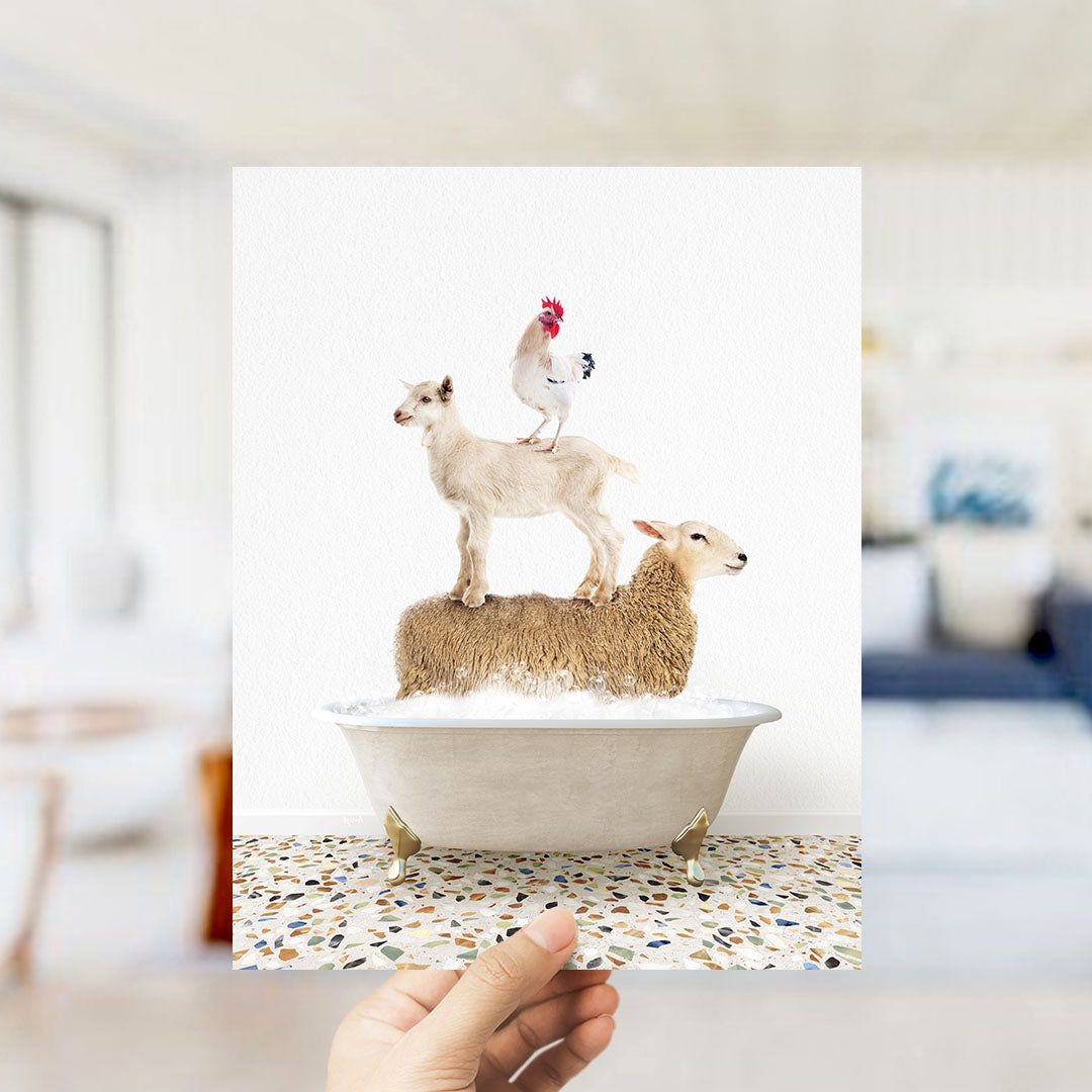 A hand holds up a framed image depicting a goat standing on a sheep's back while a chicken sits on top of the sheep.