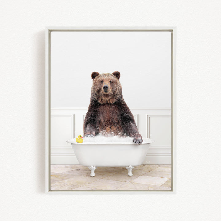A brown bear sitting in a white bathtub, with a yellow rubber duck floating in the water.