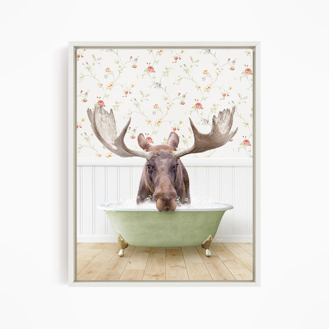 A moose with large antlers is sitting in a green bathtub, surrounded by a floral wallpaper.