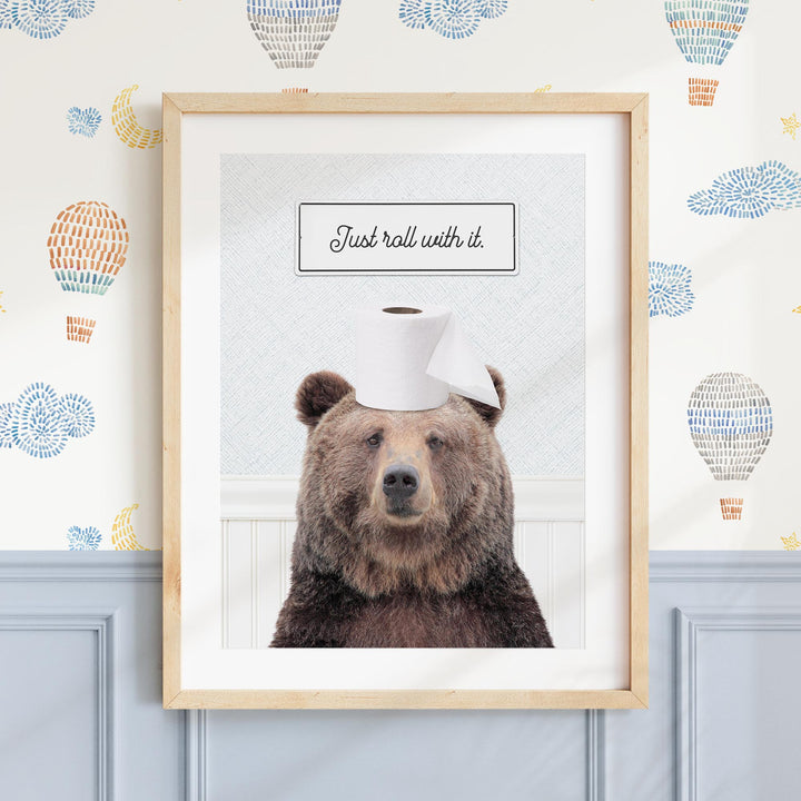 A framed image of a brown bear wearing a roll of toilet paper on its head, with the text "Just roll with it."
