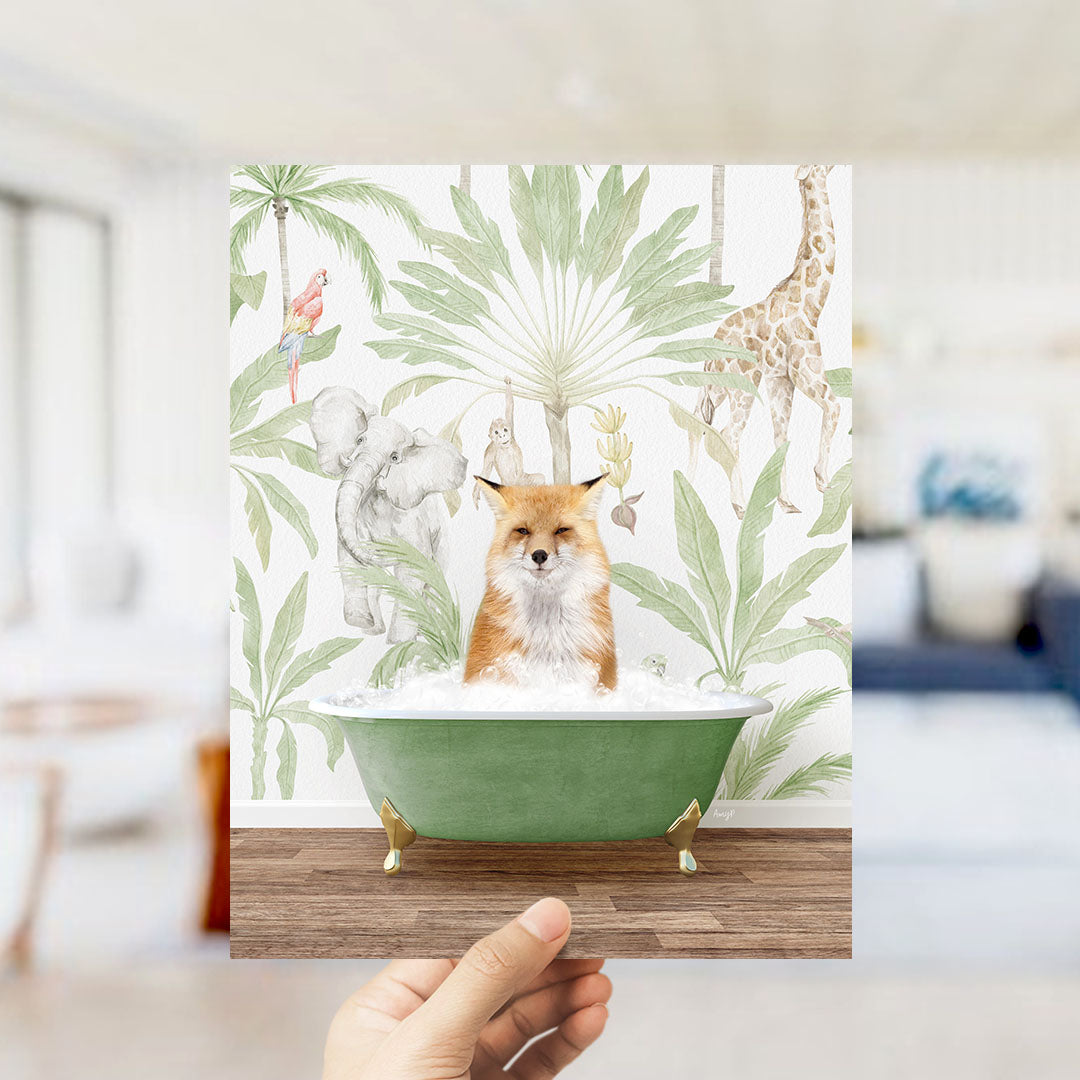 A hand holds up a framed print featuring a fox sitting in a bathtub surrounded by tropical plants and animals, including a giraffe and a parrot.