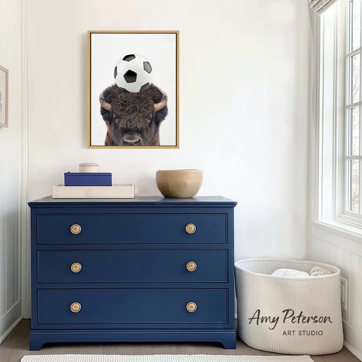 a blue dresser with a framed picture of a buffalo on top of it, and a white basket next to it. The dresser is situated in a room with a window and a white wall.