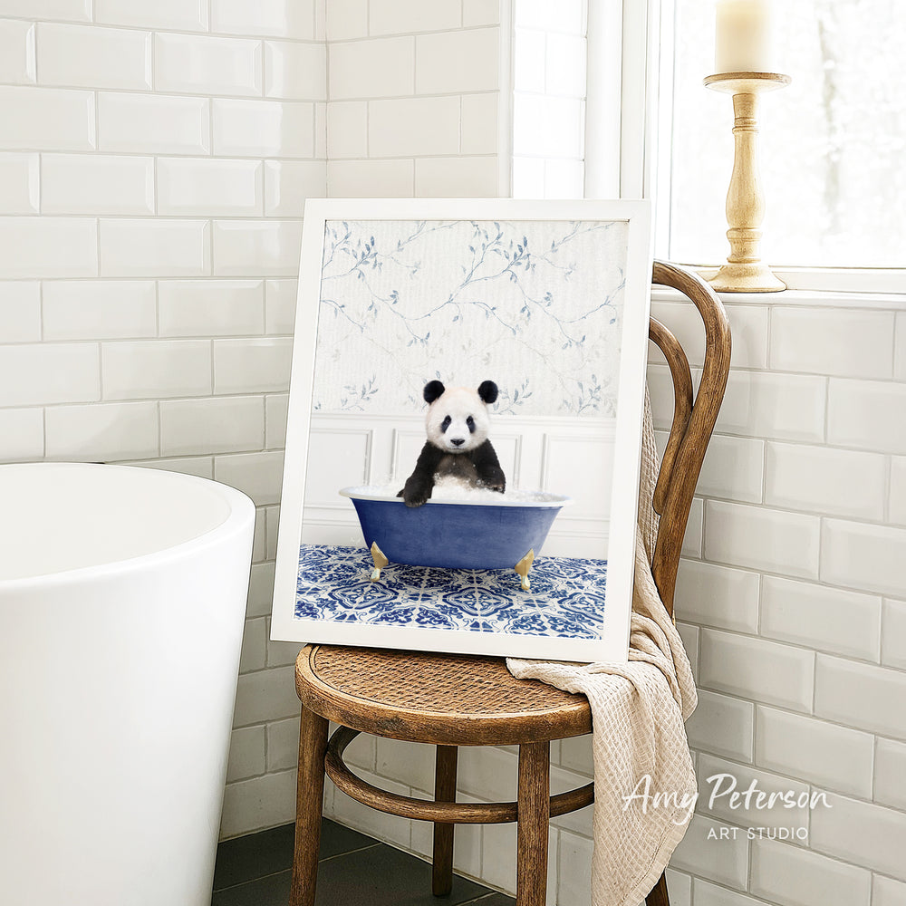 A framed image of a panda sitting in a blue bathtub is displayed on a wooden chair in a bathroom setting.