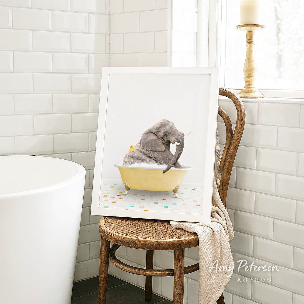 A framed image of a gray elephant sitting in a yellow bathtub, surrounded by colorful tiles, is displayed on a wooden chair in a bathroom setting.