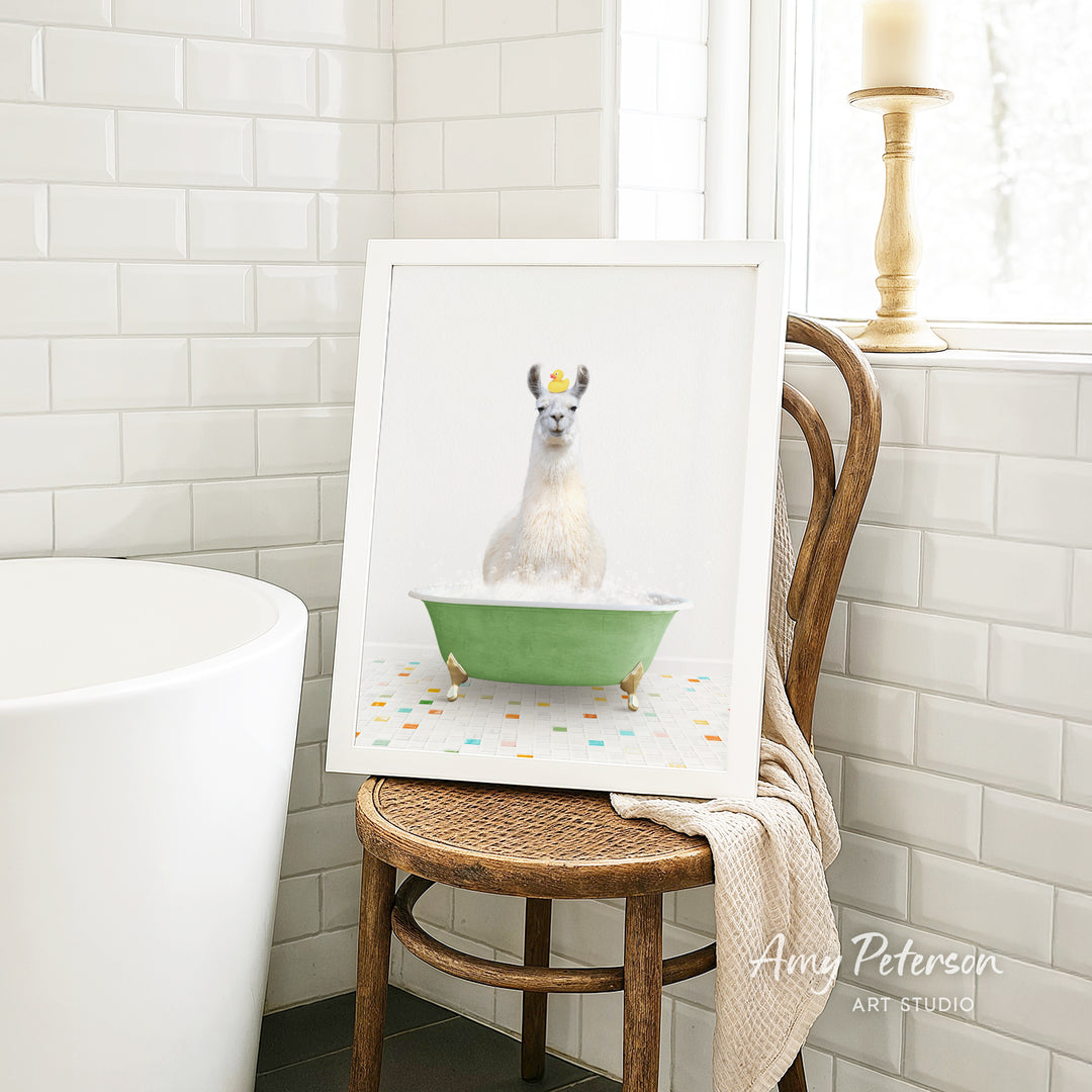 A framed image of a white llama sitting in a green bathtub, surrounded by colorful tiles, is displayed on a wooden chair in a bathroom setting.