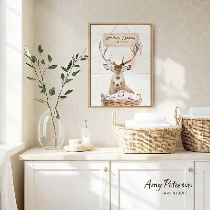 a bathroom scene with a framed picture of a deer with antlers, a wicker basket, and a vase of greenery on a white countertop.