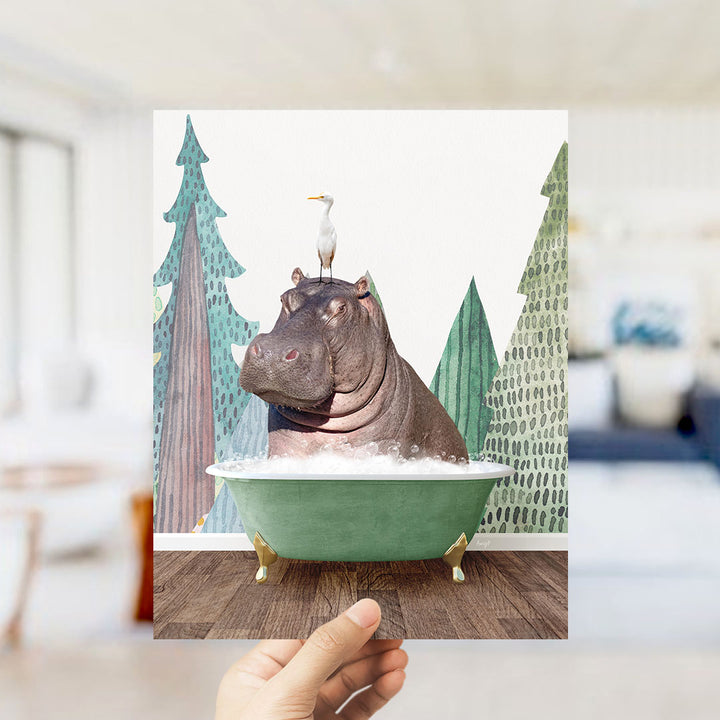 A hand holds up a framed image depicting a hippopotamus sitting in a green bathtub, with a seagull perched on its head.