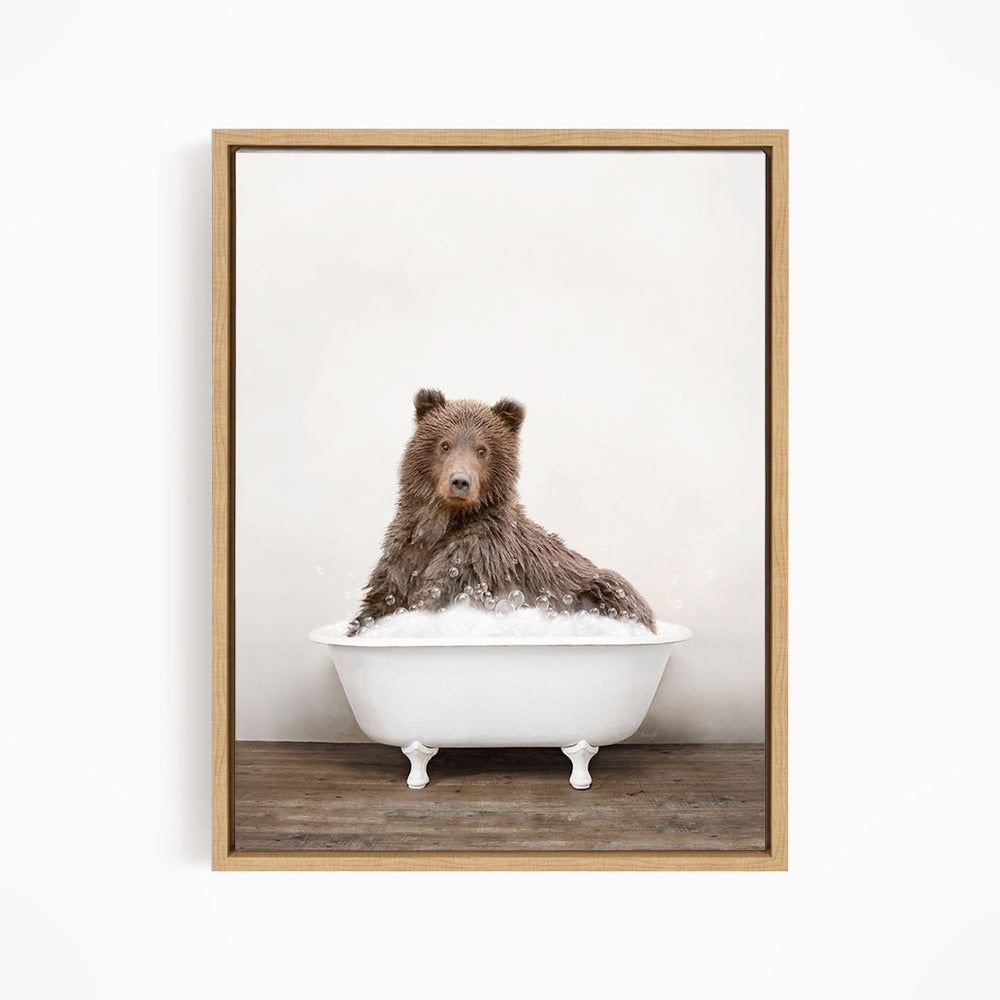 A brown bear sitting in a white bathtub filled with bubbles, looking directly at the camera.