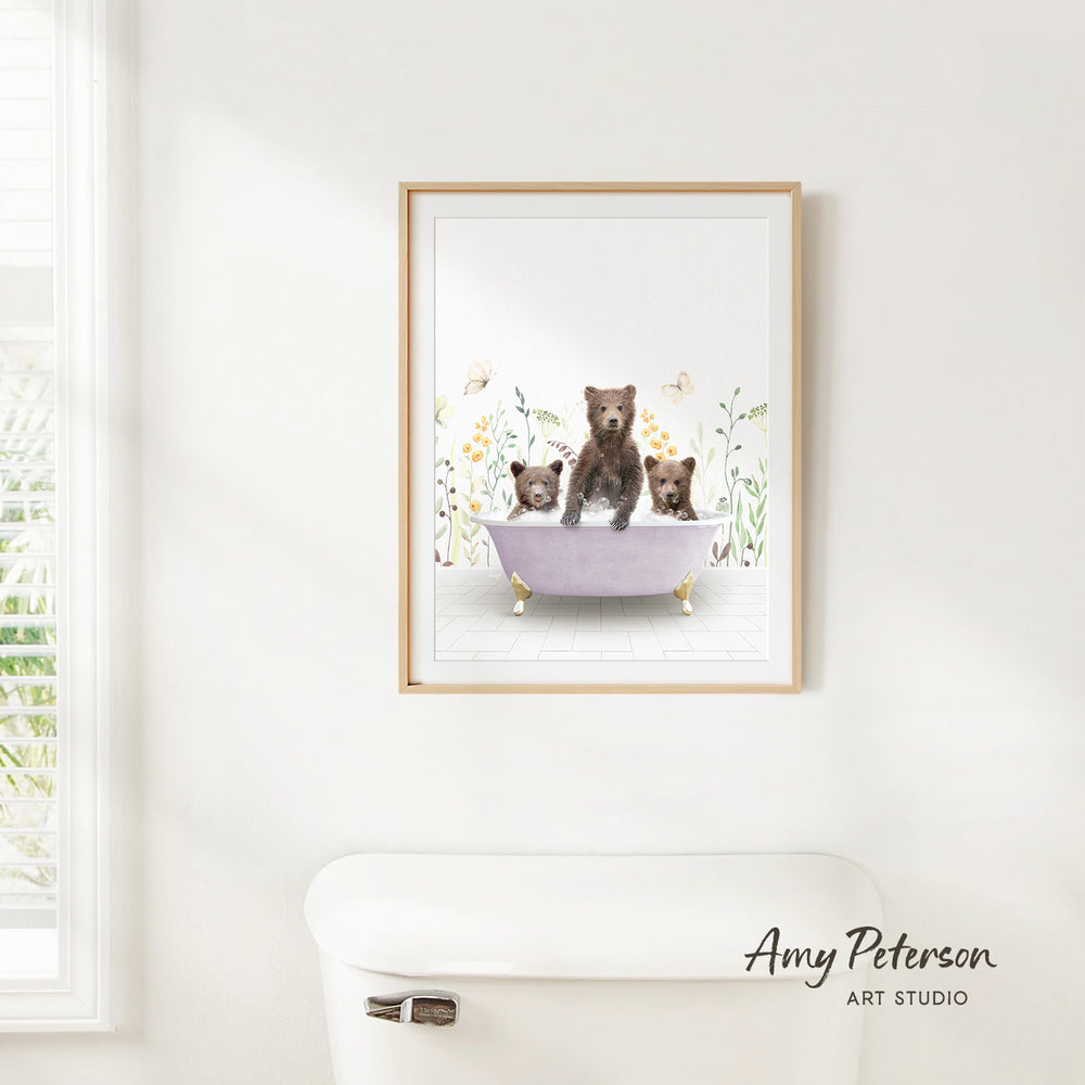 A framed illustration of three bears sitting in a bathtub, surrounded by flowers and butterflies, hanging on a white wall.