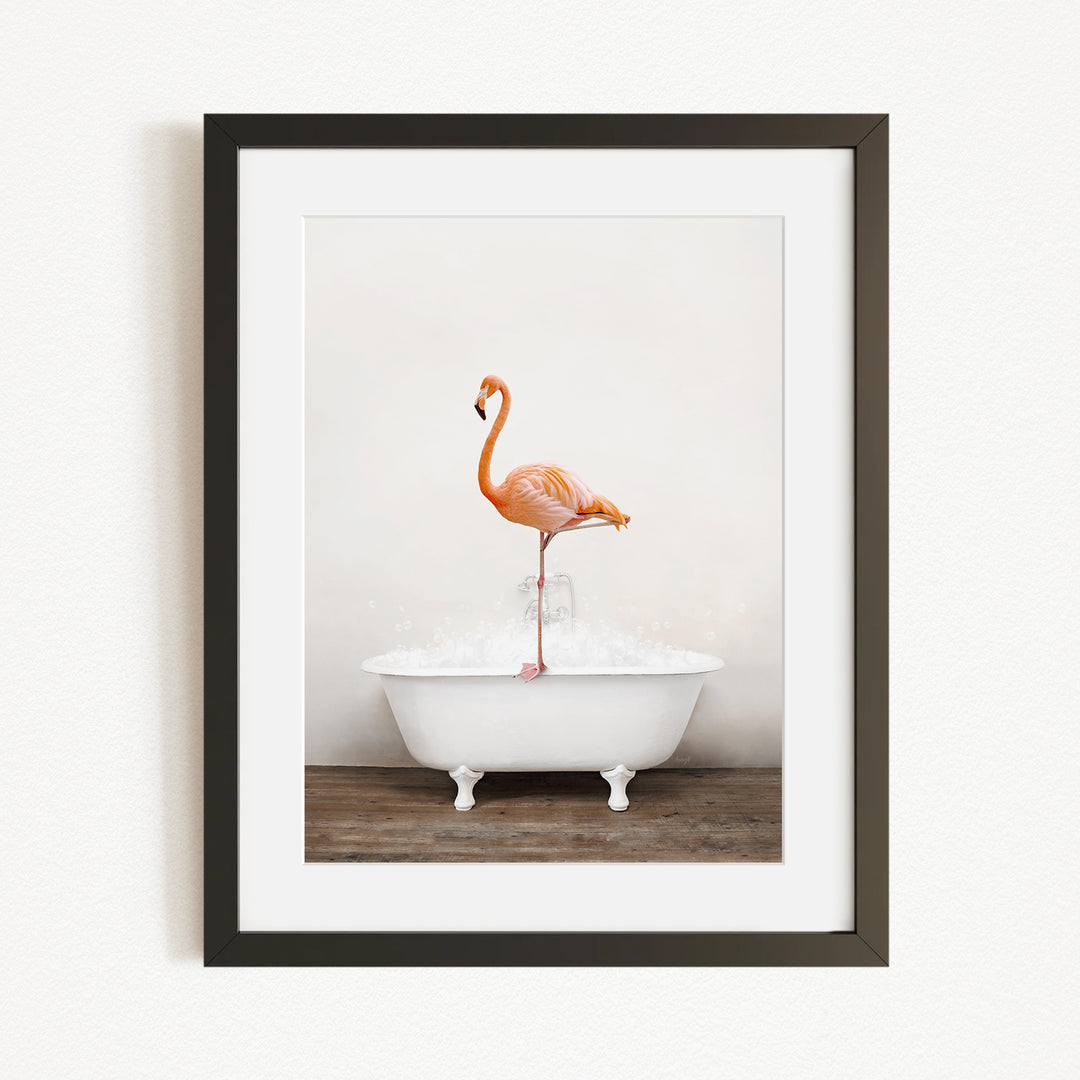 A framed image of a flamingo standing on one leg inside a white bathtub, with a wooden floor beneath it.