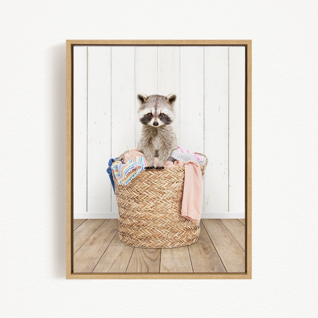 A raccoon sitting in a woven basket filled with clothes.
