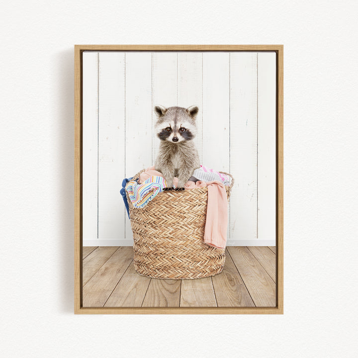 A raccoon sitting in a woven basket filled with clothes.