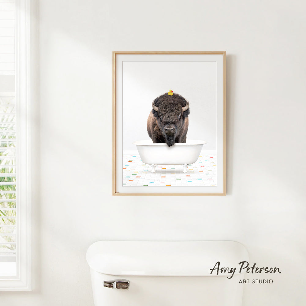 A framed image of a buffalo standing in a bathtub, with a yellow rubber duck on its head.