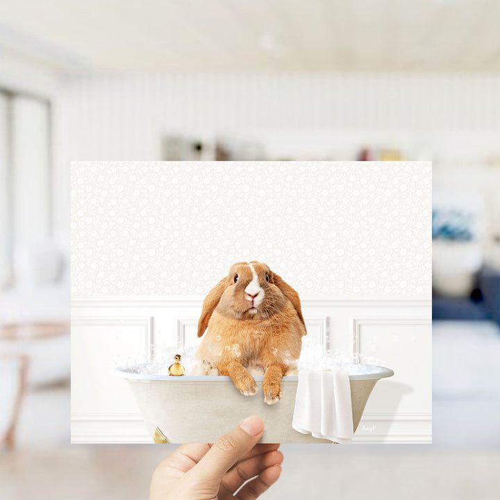A hand holding a framed image of a rabbit sitting in a bathtub filled with bubbles.