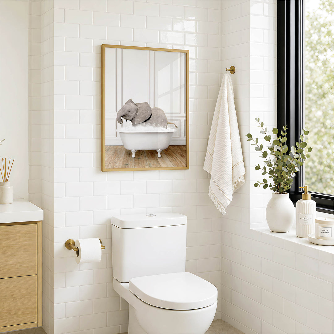 A bathroom with a white toilet, a framed image of an elephant in a bathtub, and a window with greenery on the sill.