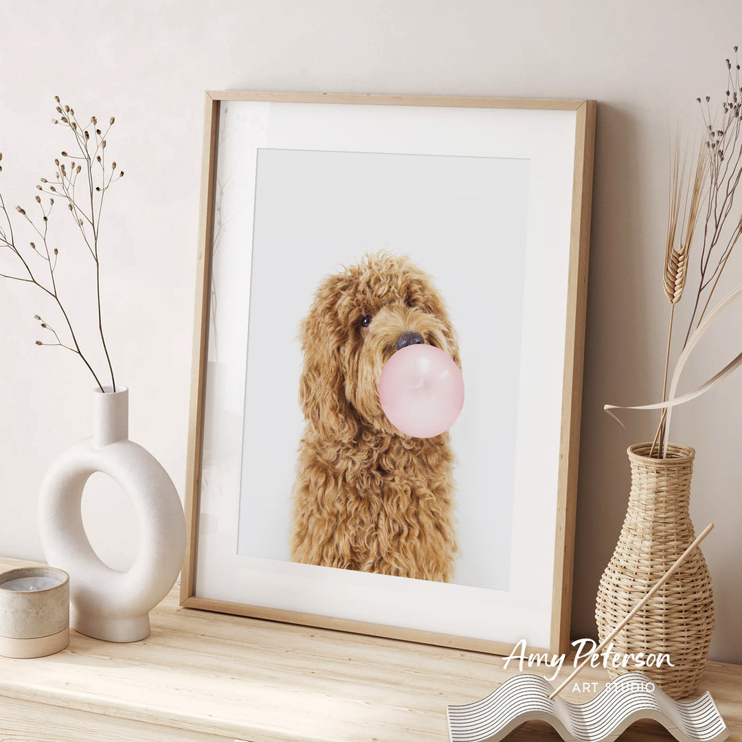 A framed photograph of a brown dog blowing a bubble gum bubble is displayed on a wooden shelf, accompanied by decorative vases and a woven basket.