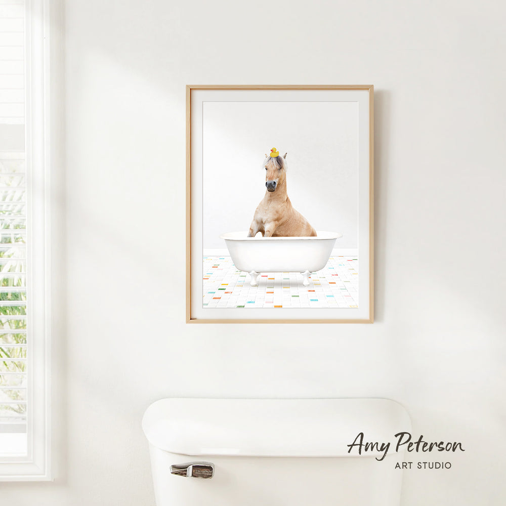 A framed image of a horse sitting in a bathtub, with a yellow flower on its head, is hanging on a white wall.