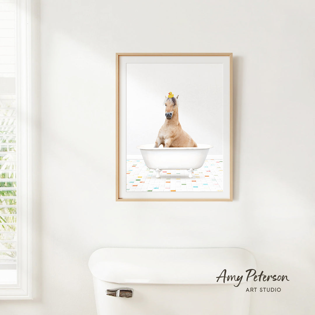 A framed image of a horse sitting in a bathtub, with a yellow flower on its head, is hanging on a white wall.