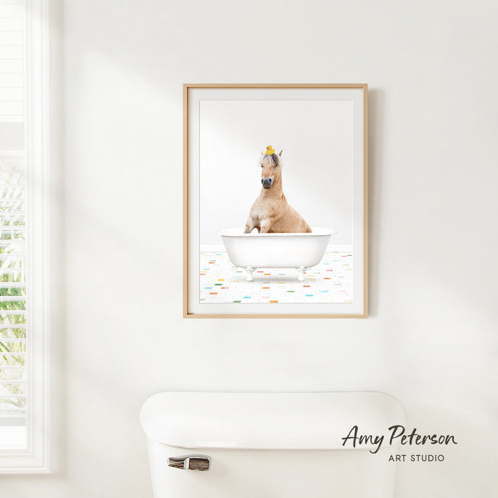 A framed image of a horse sitting in a bathtub, with a yellow flower on its head, is hanging on a white wall.