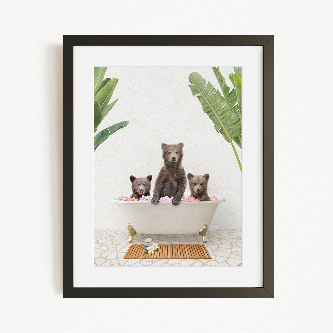 A framed image depicting three bears sitting in a bathtub filled with flowers, surrounded by tropical plants.
