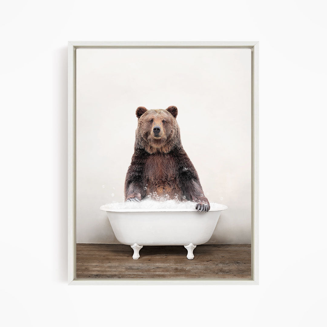 A brown bear sitting in a white bathtub filled with water, appearing to enjoy the bath.