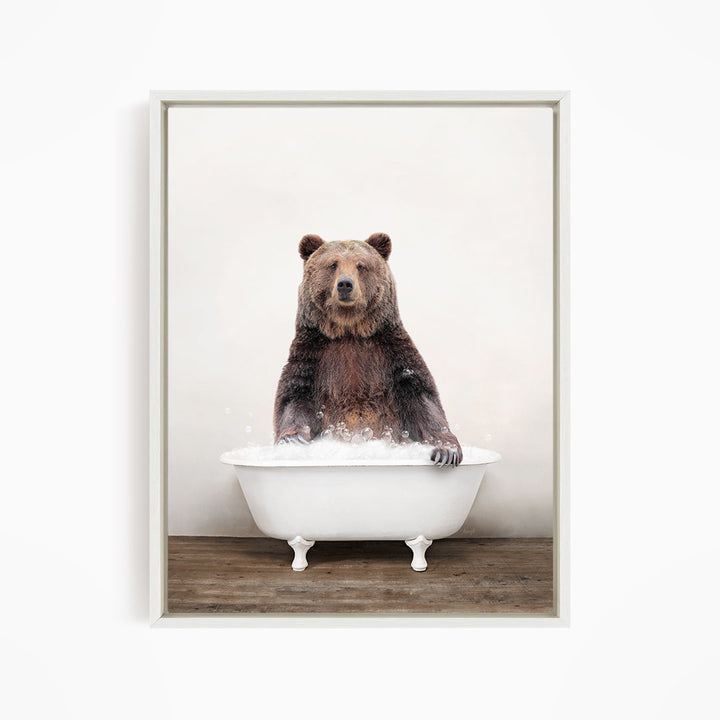 A brown bear sitting in a white bathtub filled with water, appearing to enjoy the bath.