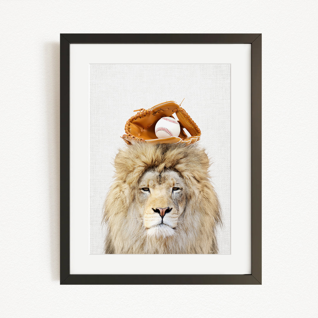 A framed image of a lion wearing a baseball glove on its head, with a baseball resting on top of the glove.