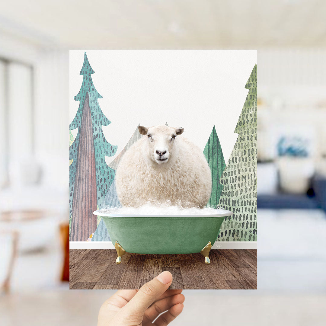 A hand holds up a framed image depicting a fluffy white sheep sitting in a green bathtub, surrounded by a winter landscape with trees and a snowy ground.